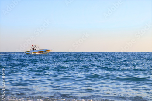 Blue sea silhouette of a Boat on the horizon. Calm sea. Beautiful seascape. Beautiful sea at sunset. Ocean and sky background. The Boat is racing on the water. Light waves. Blue water