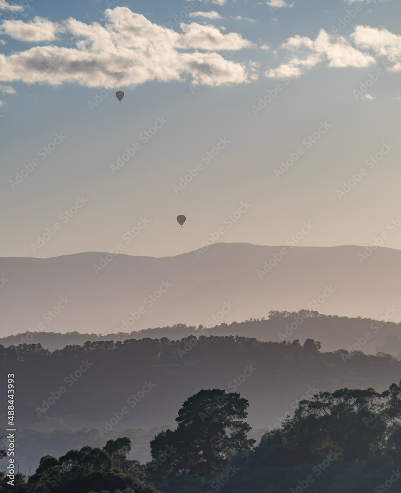 Two hot air balloons float over the Yarra Valley at sunrise