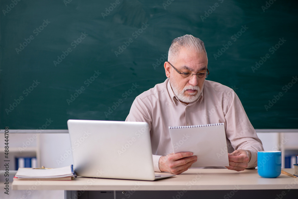 Old male teacher in front of blackboard Old male teacher in front of blackboard