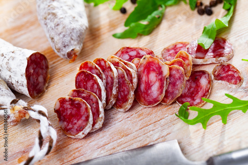 Sliced Catalan sausage Fuet on wooden table with arugula and black pepper photo