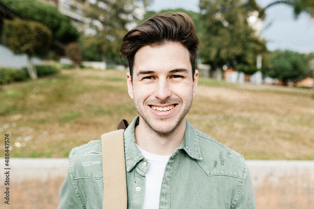 Trendy handsome young student man with backpack smiling at camera while standing at campus college