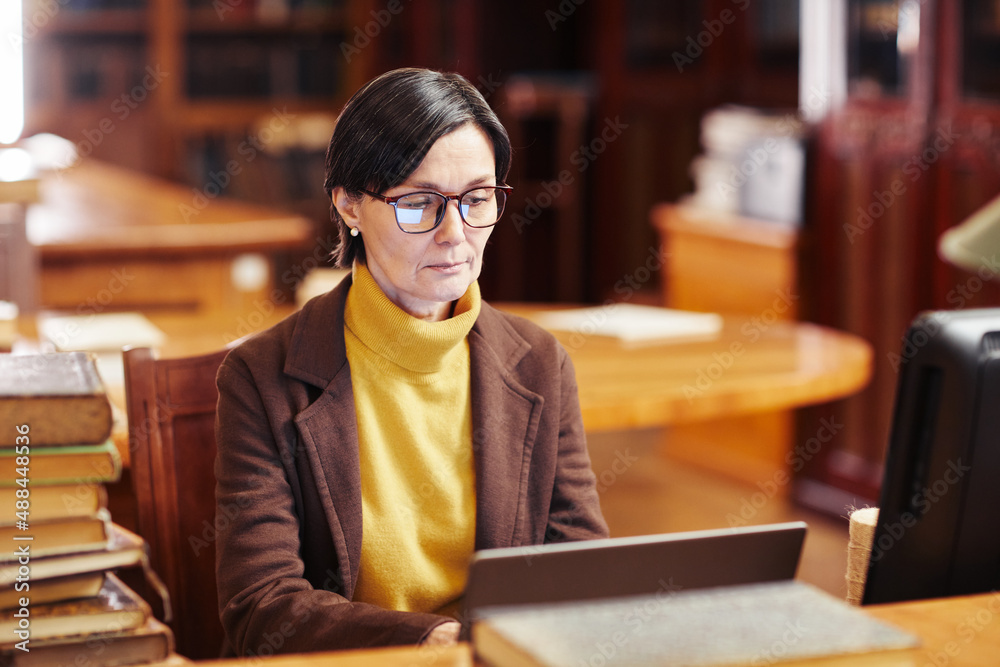 Warm toned portrait of female librarian using laptop while working with book catalogue Warm toned portrait of female librarian using laptop while working with book catalogue