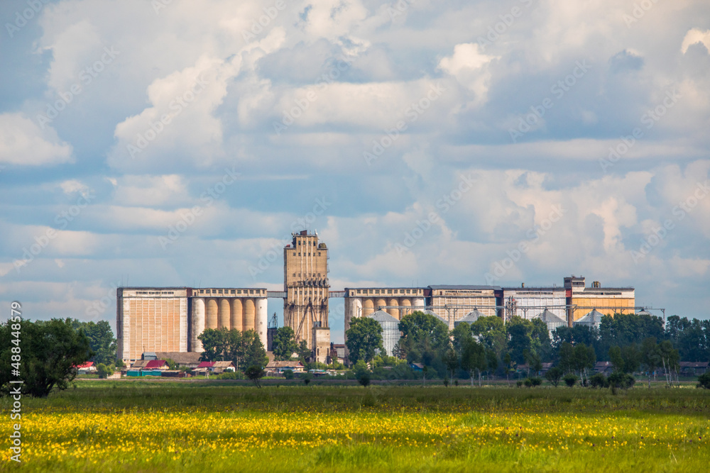 An old abandoned grain elevator stands in a green field in Russia. Abandoned grain production.