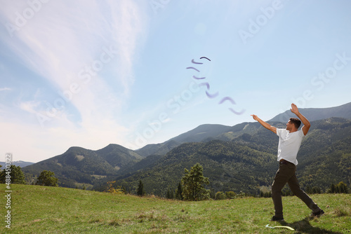 Man throwing boomerang in mountains on sunny day. Space for text