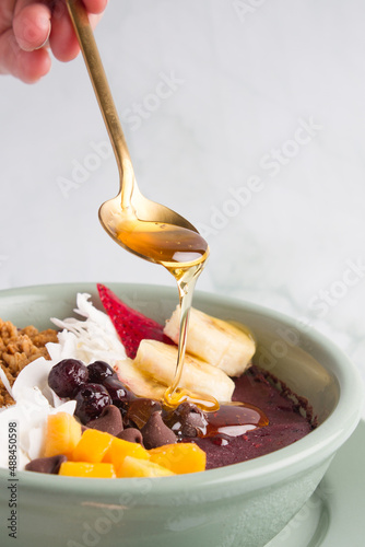 acai bowl with bananas, mango, blueberries, coconut, granola, serving honey.  marble background.