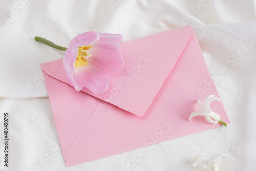 pink tulip and little white hyacinth flower and pink envelope on white bed linen, gift card, flower for anyone