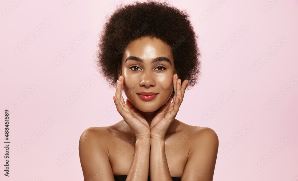 Young smiling Black woman with afro hair, gently touching facial skin with finger, concept of beauty spa and cosmetology. African american girl without makeup with glowing skin after shower, head and Young smiling Black woman with afro hair, gently touching facial skin with finger, concept of beauty spa and cosmetology. African american girl without makeup with glowing skin after shower, head and