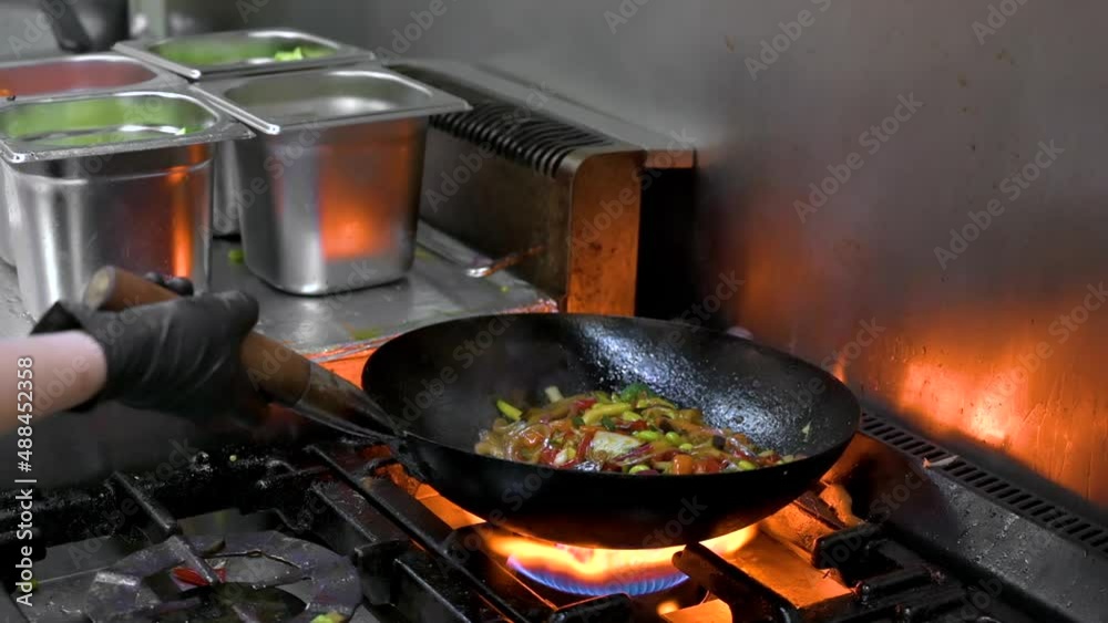 Slow motion of Chef Cookin wokg in the Kitchen. Restaurant wok fire cooking Close up, cook frying vegetable in the commercial kitchen. High quality FullHD footage