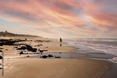 Man from behind walking alone on the beach. Sky in orange colors.