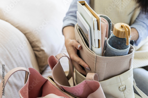 Closeup female hands shifting modern comfortable storage felt organizer into leather handbag