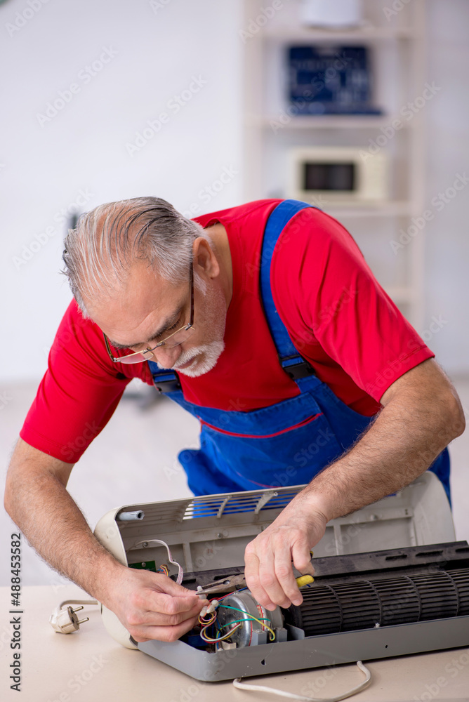 Old repairman repairing air-conditioner at workshop Old repairman repairing air-conditioner at workshop