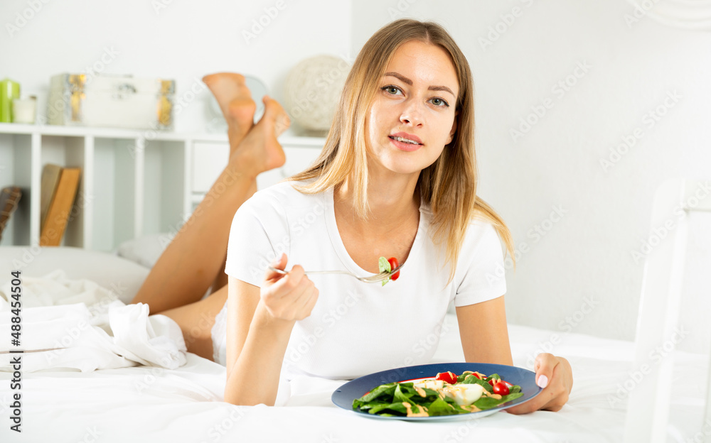 Portrait of young female in underwear eating healthy vegetable salad in bed