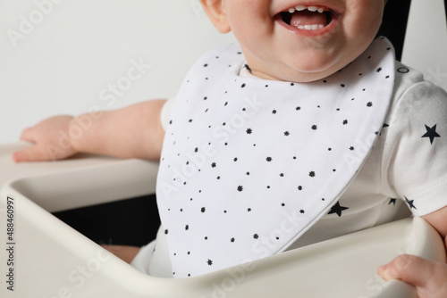 Cute little baby wearing bib in highchair on white background, closeup