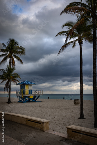 A view towards the beach from the Hollywood, Florida boardwalk with lifeguard observation shelter between silhouettes of tall palm trees