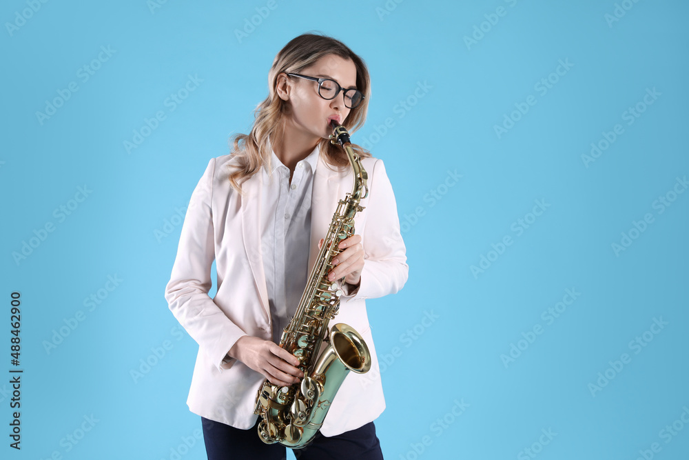 Fototapeta premium Beautiful young woman in elegant outfit playing saxophone on light blue background