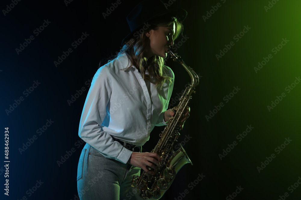 Naklejka premium Beautiful young woman playing saxophone on dark background