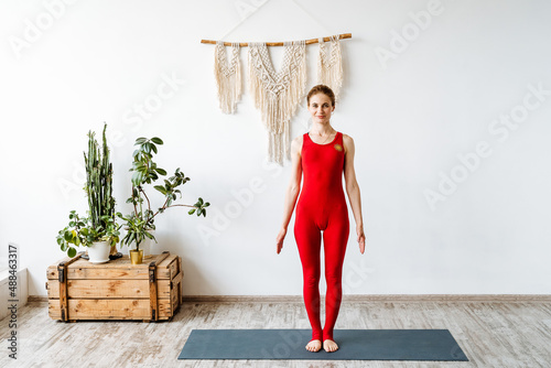 A smiling girl in a red suit performs an exercise from yoga. Stand in the pose of the mountain. Tadasana. Easy exercises for beginners. Yoga for body and soul. photo