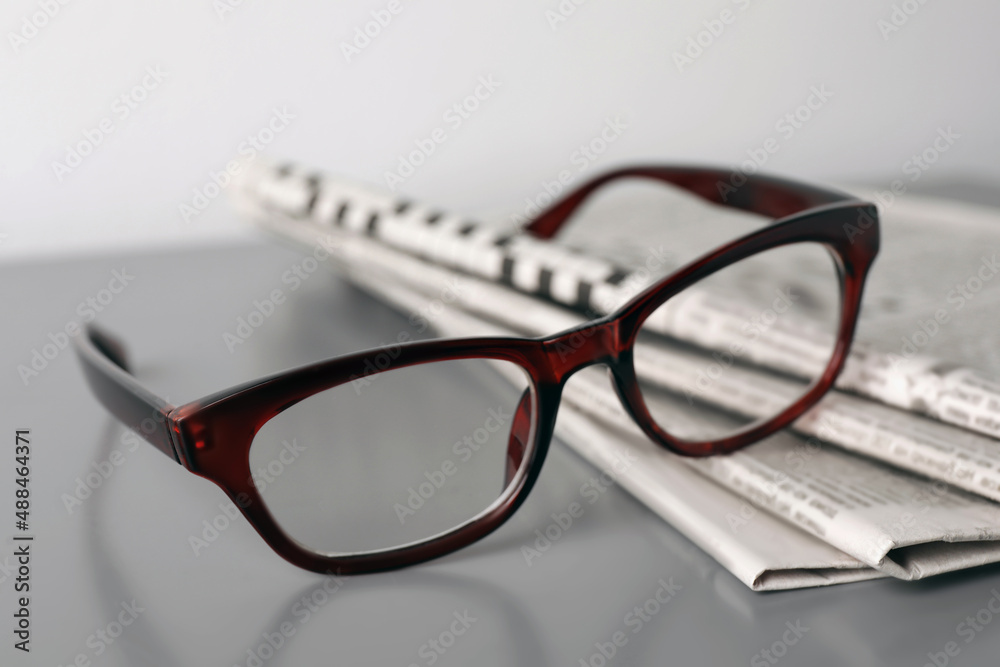 Newspapers and glasses on grey table, closeup Newspapers and glasses on grey table, closeup