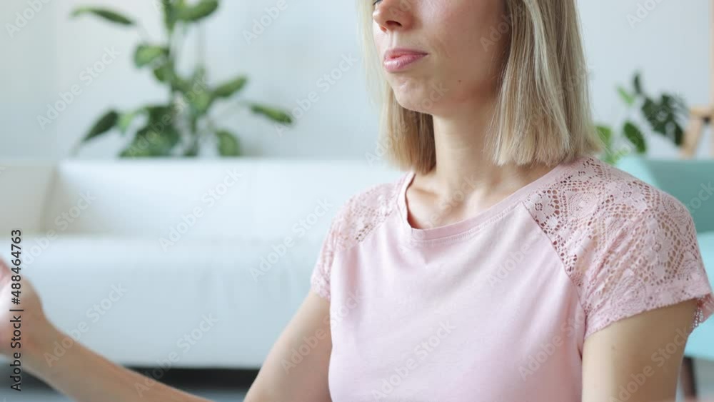 Closeup view of young female meditating and sitting on floor in home room spbi. 4k video Portrait of beautiful european woman does asana with eyes closed and joins hands in mudra, sits on mat in Closeup view of young female meditating and sitting on floor in home room spbi. 4k video Portrait of beautiful european woman does asana with eyes closed and joins hands in mudra, sits on mat in