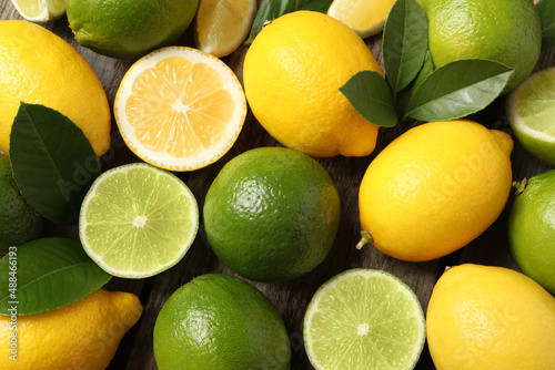 Fresh ripe lemons, limes and green leaves as background, top view