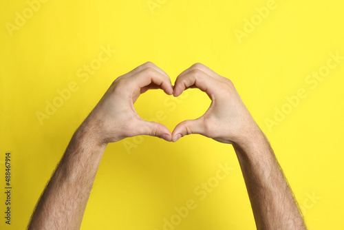 Man making heart with his hands on yellow background  closeup