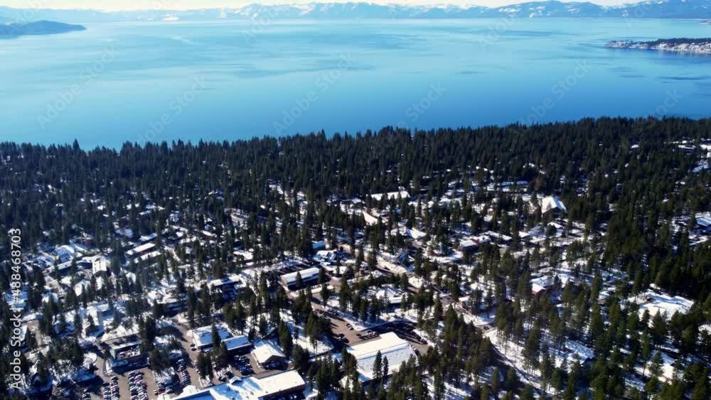 A beautiful aerial drone shot, flying over buildings in the woods towards the crystal clear lake at Lake Tahoe, Nevada-California. A beautiful aerial drone shot, flying over buildings in the woods towards the crystal clear lake at Lake Tahoe, Nevada-California.