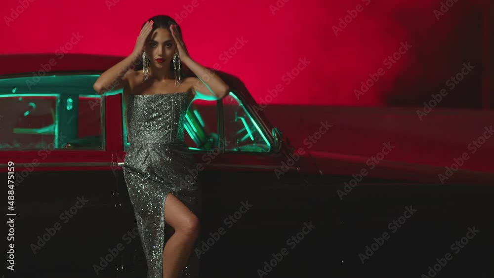 Beautiful Elegant Young Woman Standing , Dancing and Flirting near old retro classic car. Old fashioned luxury style concept . Rich fashion lifestyle . Luxury dress with fabric glitter, spangles .