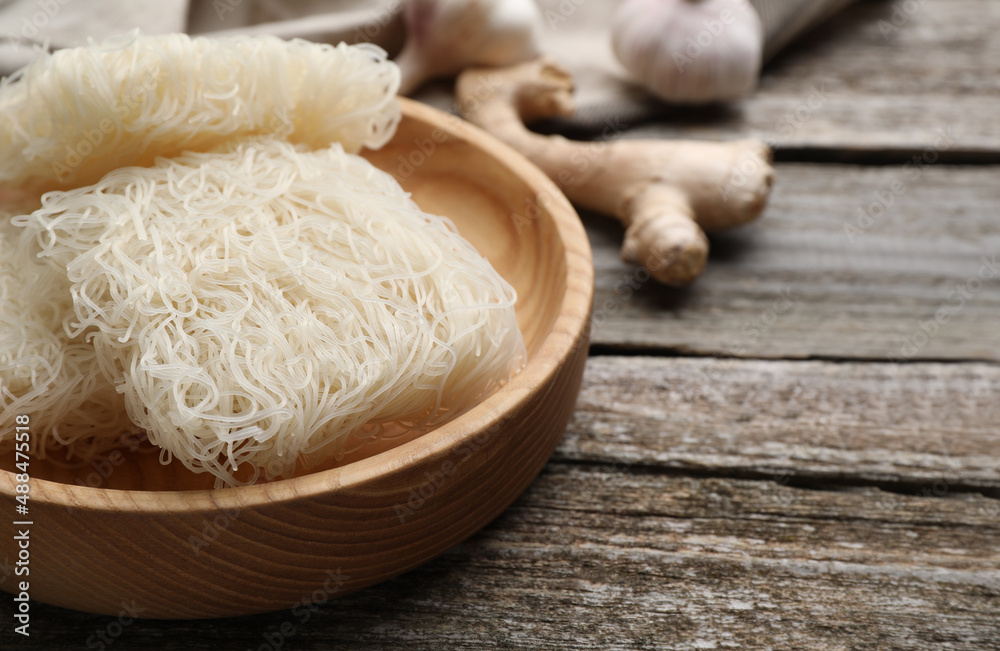 Bowl with dried rice noodles on wooden table, closeup. Space for text