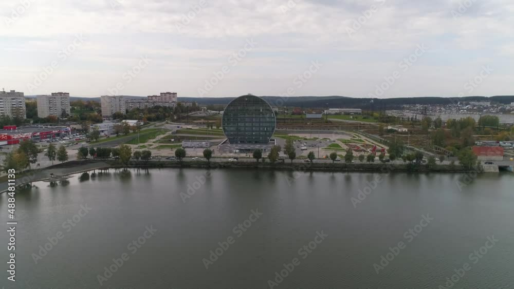 Aerial view of modern glass building in the city in the form of a washer next to a pond. Around the building there is a beautiful area with parking, children's playgrounds, walking paths and lawns. Pe Aerial view of modern glass building in the city in the form of a washer next to a pond. Around the building there is a beautiful area with parking, children's playgrounds, walking paths and lawns. Pe