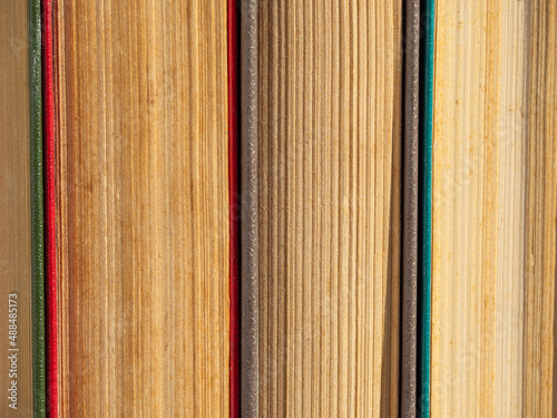 Abstract textured background of pages of closed hardcover books. Old battered books with yellowed pages from time close-up. Close-up of old books standing side by side on a bookshelf
