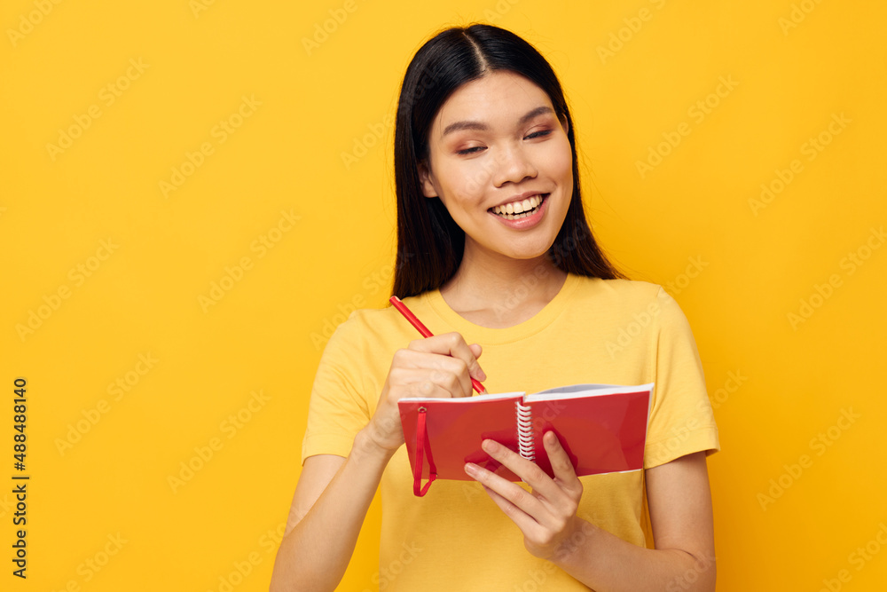 Charming young Asian woman in a yellow t-shirt red notebook training yellow background unaltered Charming young Asian woman in a yellow t-shirt red notebook training yellow background unaltered