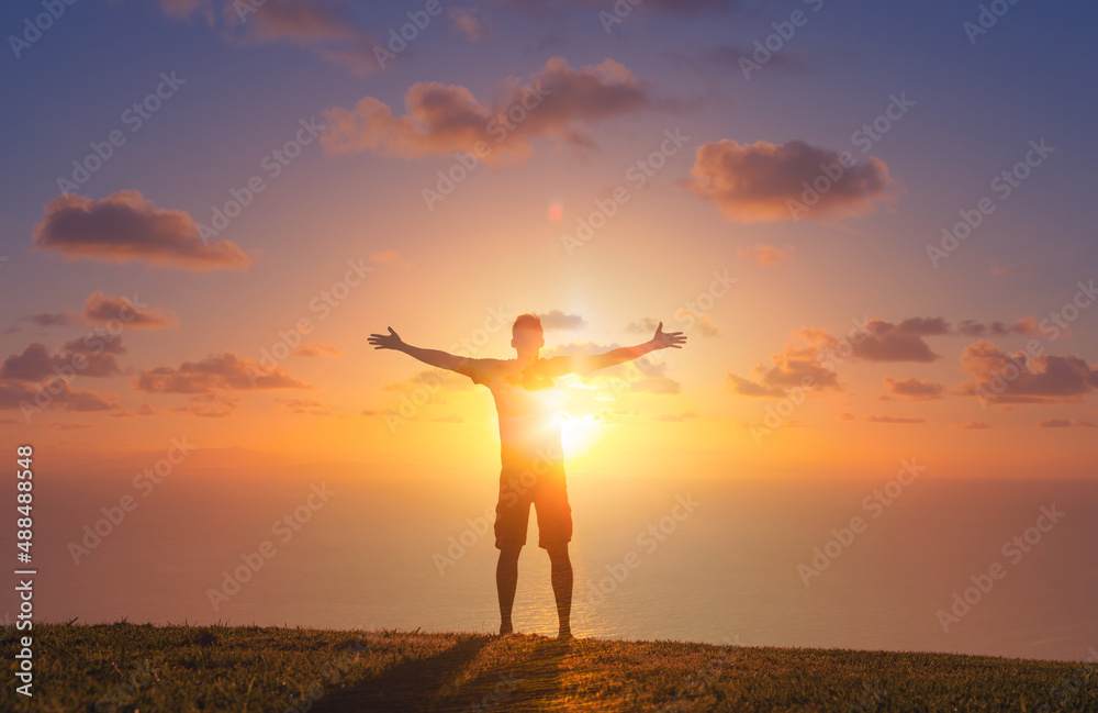 Man relaxing in a field enjoying nature with arms outstretch up to the sunrise. Feelings of hope, worship  and happiness 