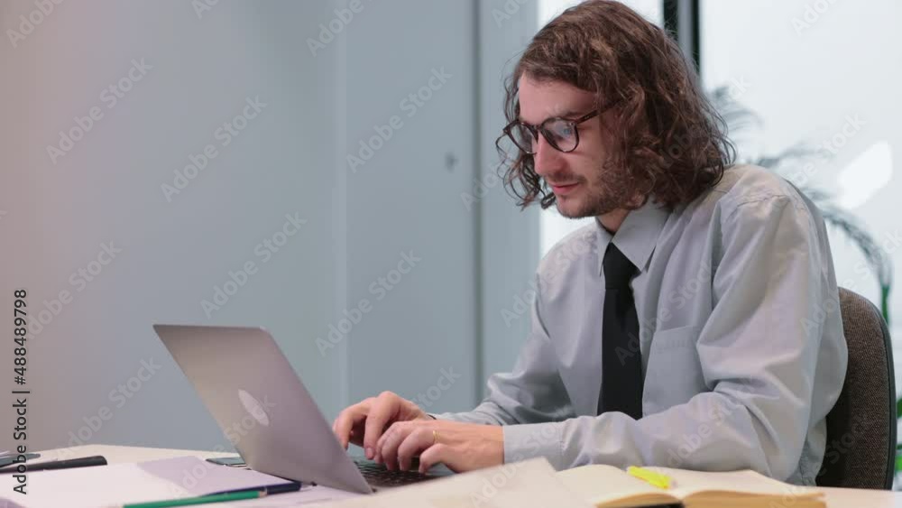 Young American businessman typing on laptop and sitting at table in company spbi. 4k video Portrait of caucasian man looks at computer screen and types with smile, does work or communicates on chat Young American businessman typing on laptop and sitting at table in company spbi. 4k video Portrait of caucasian man looks at computer screen and types with smile, does work or communicates on chat