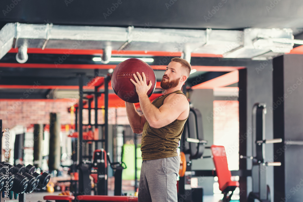 Young bearded athletic man training in the gym with a sports med ball. The concept of fitness