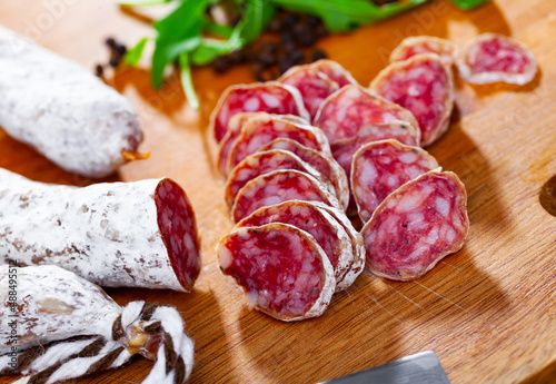 Traditional Catalan thin dry cured pork sausage Fuet sliced on cutting board with arugula and spices