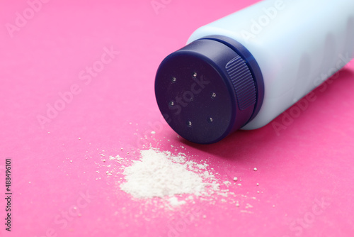 Bottle and scattered dusting powder on pink background. Baby cosmetic product