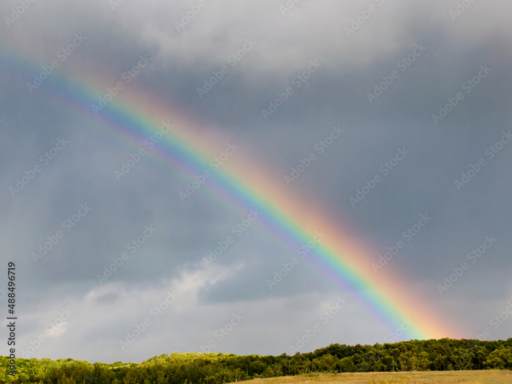 blurred, defocusing rainbow in the sky with clouds on the background of fields and forests. blurred, defocusing rainbow in the sky with clouds on the background of fields and forests.