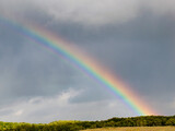 blurred, defocusing rainbow in the sky with clouds on the background of fields and forests.