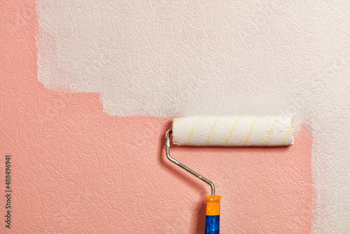 A paint roller paints a coral colored wall with white paint. Close-up. photo