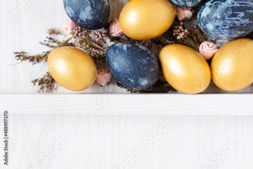 easter wooden background with golden and dark blue eggs and dried flowers with empty space for text top view