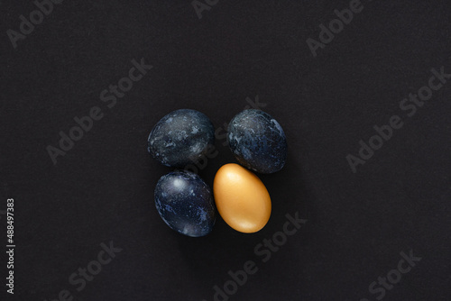 four easter eggs in blue and gold on a black paper background, conceptual easter minimalism