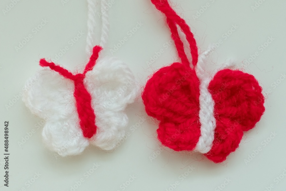 Crochet butterfly in red and white strains of yarn as martenitsa, Bulgarian folklore tradition with adornment symbols for spring in march. Shallow depth of focus, light background. Baba Marta Day. Crochet butterfly in red and white strains of yarn as martenitsa, Bulgarian folklore tradition with adornment symbols for spring in march. Shallow depth of focus, light background. Baba Marta Day.