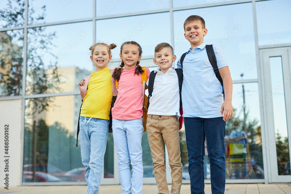 Obraz premium Smiling kids with backpacks standing near modern building