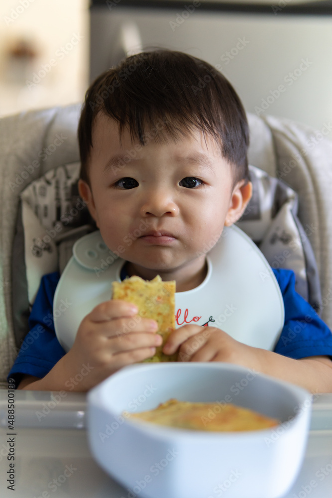 Adorable joyful and Happy 1 years old Chinese baby boy having food while sit on baby chair Adorable joyful and Happy 1 years old Chinese baby boy having food while sit on baby chair