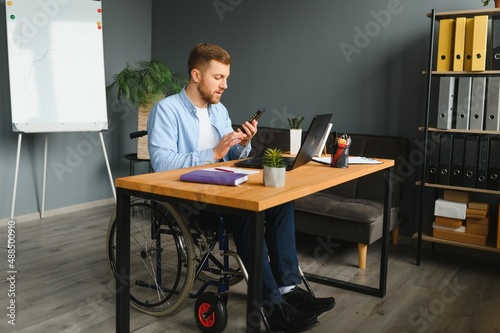 Disabled Young Businessman On Wheelchair Giving Presentation To His Colleague In Office