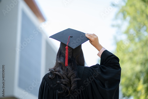 Graduation day, back view of Asian woman with graduation cap and coat holding diploma, success concept photo
