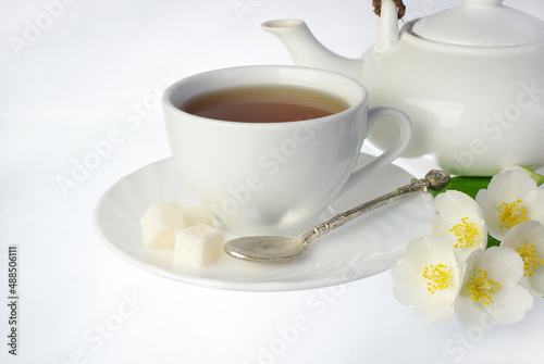 Cup of tea on a saucer, spoon, sugar and jasmine flowers on a white background.