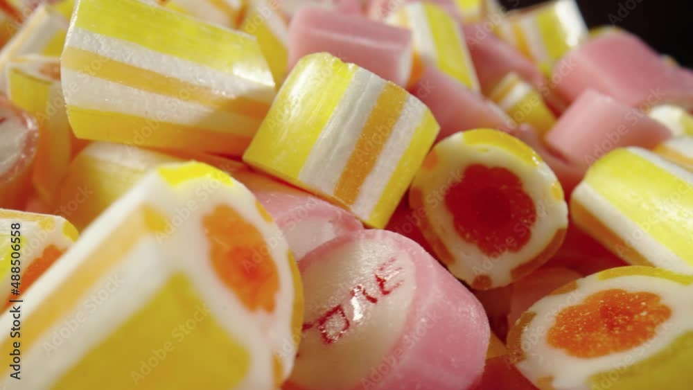 Colored striped caramel candies with the inscription Love rotating on black background. Mix of pink and yellow lollipops close up. Candy Shop. Festive background for a holiday or children's birthday. Colored striped caramel candies with the inscription Love rotating on black background. Mix of pink and yellow lollipops close up. Candy Shop. Festive background for a holiday or children's birthday.