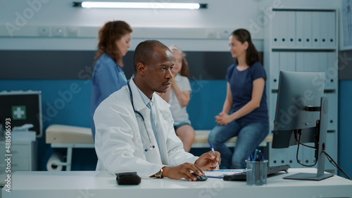 African american physician with stethoscope working on computer in medical office. General practitioner wearing white coat to plan checkup appointment on monitor  helping with recovery.