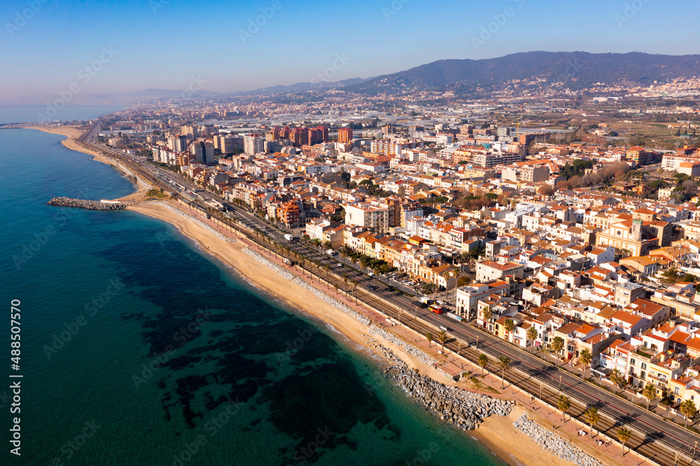 Scenic aerial view of coastal area of Spanish city of Vilassar de Mar overlooking brownish roofs of buildings and sandy seashore on sunny winter day, Catalonia